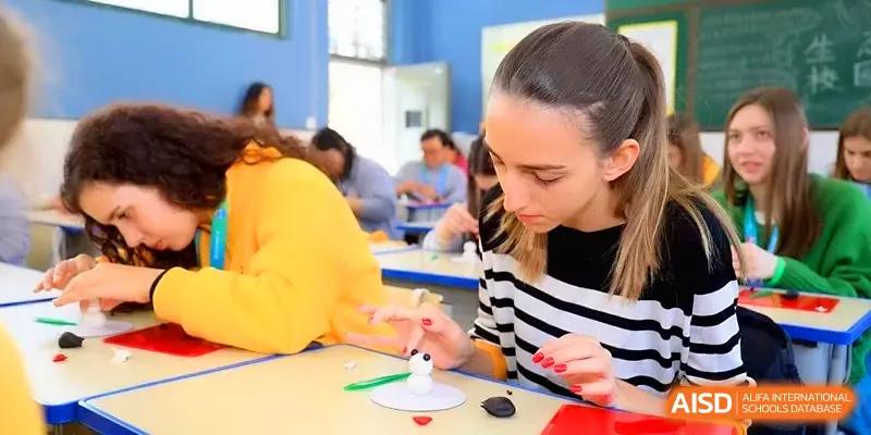 A young woman focuses on a delicate craft project at a yellow table during a cultural exchange workshop at Zhengzhou No.11 High School.