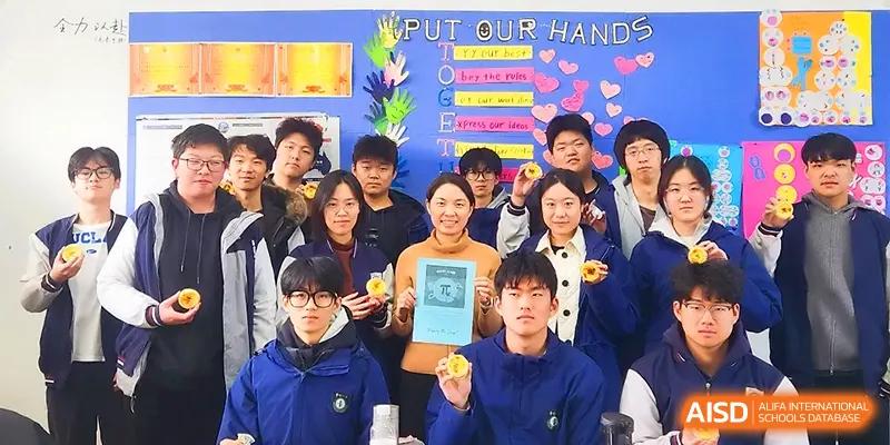 A group of smiling students and a teacher hold up handmade crafts in front of a colorful "Put Our Hands" display at Zhengzhou No.11 High School.