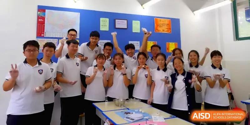 Students in a science lab smile and hold up small experiment samples in front of a blue bulletin board at Zhengzhou No.11 High School.