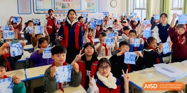Excited students in a classroom hold up blue and white tie-dye art projects they have just completed at Zhengzhou No.11 High School.