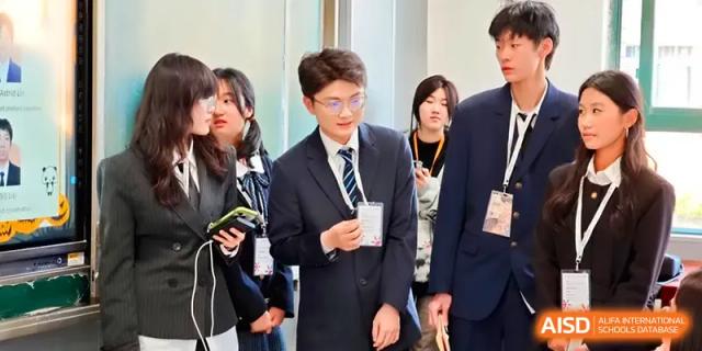 A male student in a suit and tie stands among peers during a formal school event or conference at Zhengzhou No.11 High School.