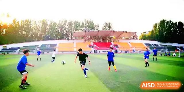 A student athlete in a blue jersey dribbles a soccer ball across a green field during a match at Zhengzhou No.11 High School.