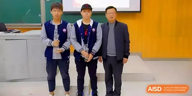 Two students and a teacher pose with a trophy, celebrating a successful competition result at Zhengzhou No.11 High School.