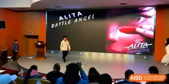 A performer walks across a stage in front of a large screen during a "Battle Angel" themed event at Zhengzhou No.11 High School.
